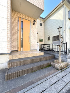 階段で高低差を活かしたアプローチが特徴的な、明るい色合いの玄関です。
