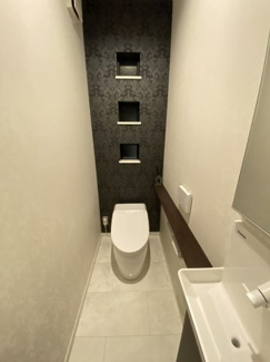 節水型のタンクレストイレを採用。ホワイトを基調とした空間に、アクセントクロスと収納棚を備え付けることで快適な空間になっております。