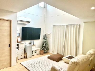 吹き抜けの天井が開放感を演出しています。白を基調とした明るいリビングに大型テレビが設置されています。家具やカーテンも統一感があり落ち着いた雰囲気です。収納スペースも豊富に確保されています。