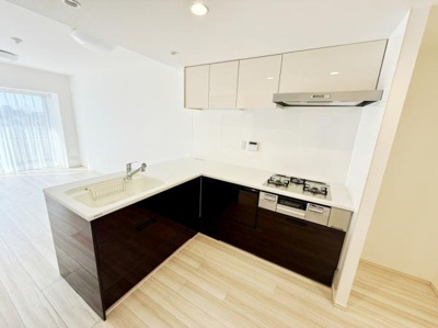 明るい空間に調和するシンプルなデザインのキッチンです。収納が豊富で動線もスムーズです。ガスコンロや換気扇など設備も整っています。天井や床の色合いが一体感を演出しています。