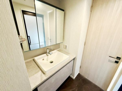 洗面台は広々としたカウンターで日々のお手入れがしやすいです。収納スペースもしっかり確保されています。落ち着いた色合いの床が空間に上品さを加えています。大きな鏡が設置されており身支度に便利です。