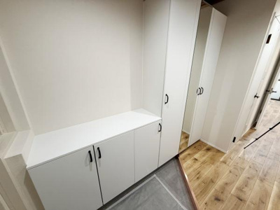 白を基調とした収納が設置され清潔感のある玄関です。大容量のシューズボックスが備わっています。フローリングとの組み合わせがすっきりとした印象を与えます。姿見鏡もあり外出前のチェックに便利です。