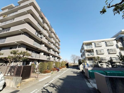 明るい青空の下建物が規則的に並び開放感のある通りが広がっています。敷地内の緑も手入れされています。外観は清潔感があり静かな雰囲気が感じられます。幅広い道路があり住環境も整っています。