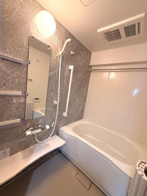 スタイリッシュなデザインのバスルームです。明るい照明が空間をすっきりと見せています。鏡や手すりカウンターなど使いやすさも考えられた設備が揃っています。浴槽も広めでゆとりを感じられる仕様です。