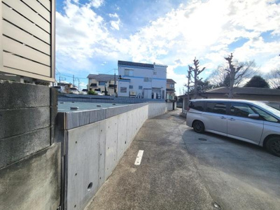 前面道路がしっかりと舗装されており車の出入りがしやすい造りです。周囲に住宅が立ち並び整った街並みが感じられます。駐車スペースも確保されています。日当たりを感じる現地写真です。