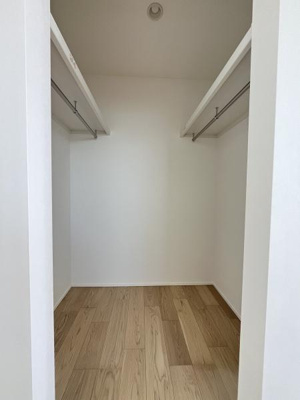 シンプルなデザインの収納スペースです。両サイドにハンガーパイプが設置されています。床は明るい木目調になっています。白い壁で清潔感があります。