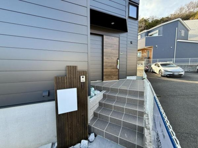 玄関部分は落ち着いた色合いで統一されています。木目調のドアが印象的なアクセントになっています。屋根付きなので天候に左右されにくく明るい光が差し込む空間です。タイル敷きで手入れも簡単です。