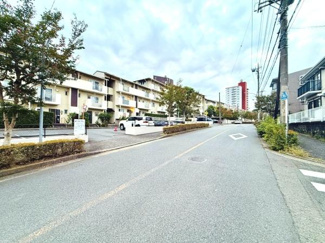 道路沿いに面した建物で整備された歩道や植栽があるのが特徴です。周囲は落ち着いた雰囲気で広々とした車道が確保されています。複数階建ての集合住宅が並び住環境が整っています。遠くには高層の建物も見えます。
