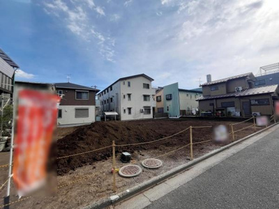 前面道路に面した現地写真です。周囲に住宅が立ち並ぶ落ち着いた雰囲気が特徴です。明るい空の下開放的な区画の様子がご覧いただけます。現地の状態がわかりやすい写真です。