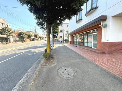 角地に位置しているため開放感と視認性があります。大きな窓が特徴で外からの明るい日差しを感じられます。歩道が広く周囲に植栽も見られます。建物の外壁とレンガタイルが調和した印象を与えています。