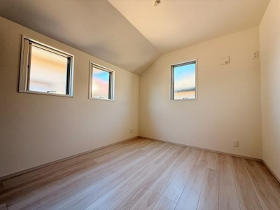 3つの窓から自然光がしっかりと入る開放的な洋室です。天井の傾斜が空間にアクセントを加えています。白を基調とした内装でどんな家具とも合わせやすい雰囲気です。フローリングが清潔感のある印象を与えます。