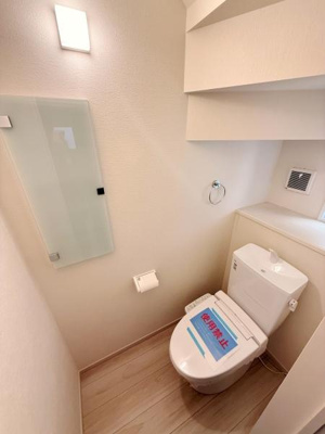 清潔感のあるトイレ空間です。壁面には手洗いスペースがあり使い勝手の良さが感じられます。窓からの採光で明るくナチュラルな床材が印象的です。収納スペースも確保されています。