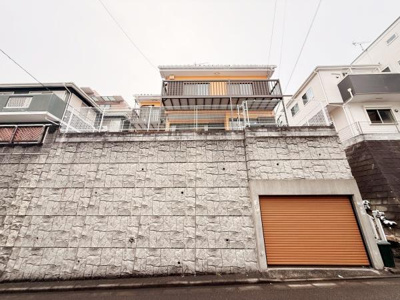 高台に位置した住まいで眺望を楽しむことができます。ワイドなバルコニーが印象的な外観です。シャッター付ガレージが設けられておりお車をしっかり収納できます。堅牢な石垣が防犯性を高めます。