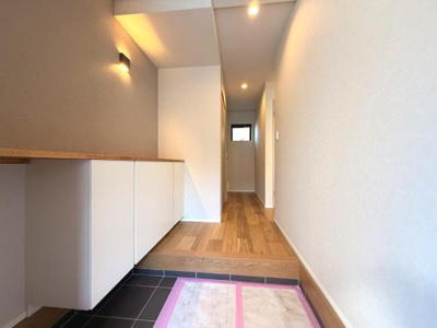 玄関は明るい照明とシンプルな色合いで清潔感のある印象です。収納スペースも確保されており整理整頓しやすい設計です。奥行きのある廊下が広がりを感じさせます。フローリングの素材感が温かみを演出しています。