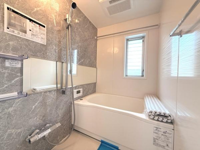 グレー調のアクセントパネルが印象的なバスルームです。大きなミラーが空間を広く感じさせます。浴室暖房乾燥機付きで一年中快適です。窓付きで換気もしやすい仕様です。シンプルで清潔感のあるデザインです。