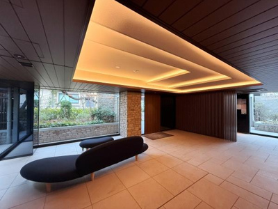 天井の間接照明がロビー全体をやわらかく照らしています。ガラス越しに外の緑が見え開放感があります。ベンチのデザインもシンプルで空間に調和しています。