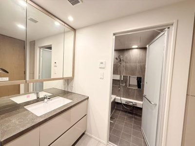 広々とした洗面台は収納力もあり使い勝手が良い空間です。大きな鏡があり採光も十分です。バスルームへ直接アクセスできる動線も便利です。清潔感のあるデザインが特徴的です。