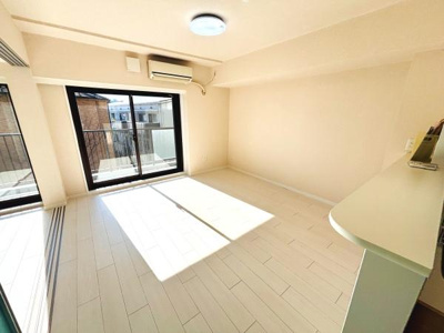 明るい日差しが差し込むリビングです。ナチュラルな色合いの床が空間を広く感じさせます。エアコンが設置されており快適にお過ごしいただけます。大きな窓からバルコニーへのアクセスも便利です。