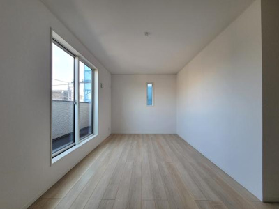 大きな窓から自然光がたっぷり差し込む洋室です。床はナチュラルな色合いで落ち着いた雰囲気を演出します。壁と天井はシンプルなホワイトで空間がすっきりしています。縦長の小窓がアクセントとなっています。