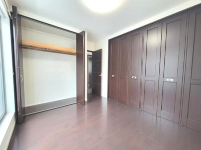 落ち着いた色合いのフローリングが特徴の洋室です。大きなクローゼットがあり収納力に優れています。窓があり明るい印象の空間となっています。扉や収納のデザインも統一感があります。