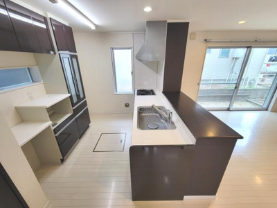 ダークブラウンの収納が印象的なキッチンです。対面カウンターがあり開放的な空間となっています。窓からの採光で明るさも確保されています。広々としたレイアウトなので使い勝手も良好です。