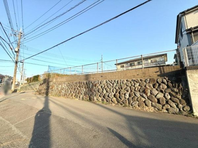 前面道路は広々としており車の通行もスムーズです。道路沿いの石垣がしっかりとした印象を与えます。周囲は開放感があり陽当たりも良好です。静かな環境で落ち着いた雰囲気が感じられます。