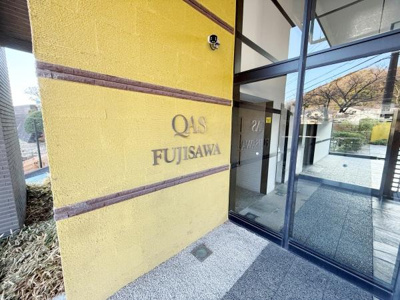 エントランスはガラスドアとイエローの外壁が印象的です。館名サインが正面に配置され訪れる方にもわかりやすい設計です。セキュリティカメラも設置されており安心感があります。建物のデザインが目をひきます。