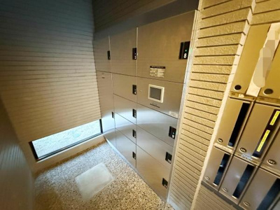 宅配ボックスが設置されており荷物の受け取りに便利です。明るい共用スペースが確保されています。共用部の清潔感が感じられます。管理が行き届いた印象のエントランスです。