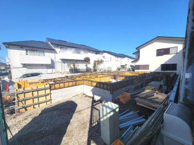 新築工事中の現場が確認できる写真です。基礎部分がしっかりと施工されており今後の進捗が期待されます。周囲には住宅も立ち並び落ち着いた雰囲気が感じられます。青空の下で作業が進んでいる様子が伝わります。