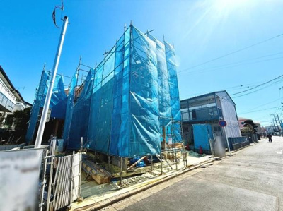 現在建設中の物件の外観写真です。周辺には住宅やアパートが立ち並んでいます。工事の進捗や形状がしっかりと確認できます。これから完成に向けての変化を楽しみにできます。道幅や前面道路の様子も確認できます。