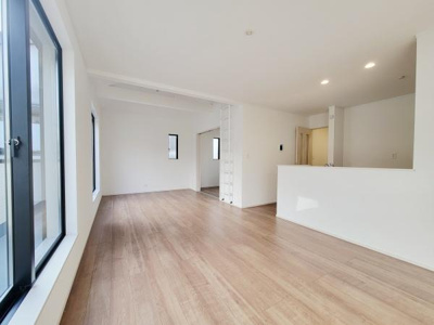 大きな窓から光が差し込むリビングです。白を基調とした内装で清潔感があります。床材の色合いがやさしい雰囲気を演出します。広々とした空間設計です。キッチンとリビングが自然につながっています。