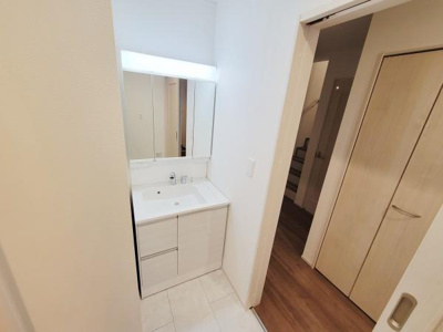 シンプルなデザインの洗面台が特徴です。明るい照明付きのミラーで使いやすさが感じられます。収納スペースも備わっているため整理整頓に役立つ仕様です。