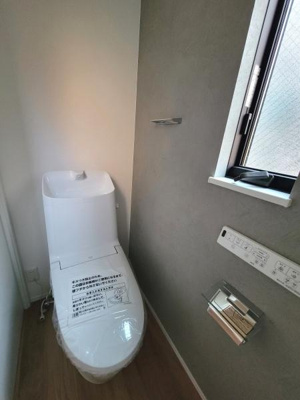 窓があり明るい空間を確保したトイレです。壁のコントロールパネルとペーパーホルダーがすっきりと設置されています。コンパクトな設計で使いやすさを追求した印象です。清潔感のある白を基調としたデザインです。