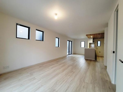 リビングはシンプルなデザインで開放感があります。窓から自然光がしっかりと入ります。床の色合いが明るさを演出しています。キッチンとのつながりもスムーズで動きやすい空間です。