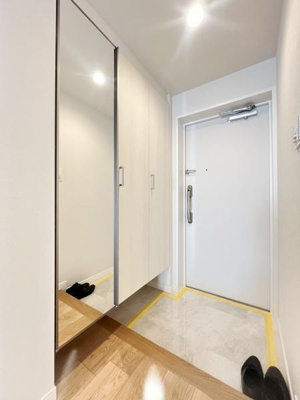 玄関には大きな収納が設置されており靴や小物もすっきり片付けられます。明るい照明が空間を引き立てています。床材の切り替えがアクセントとなっており清潔感があります。鏡面仕様の扉が広がりを感じさせます。