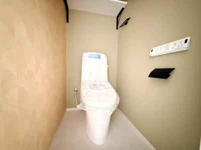シンプルで落ち着いた色合いのトイレです。壁際のリモコン操作も便利です。コンパクトな空間にまとまっています。
