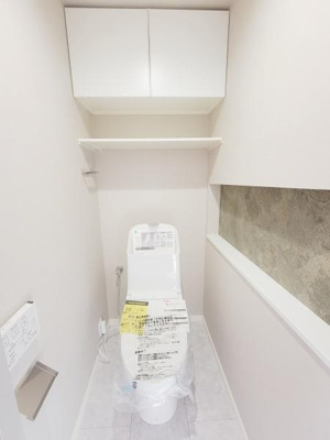 清潔感のある明るいトイレ空間です。上部には収納棚が設置されており日用品の整理にも便利です。カウンター部分がアクセントとなりすっきりとした見た目です。壁面のデザインが落ち着いた印象を与えます。