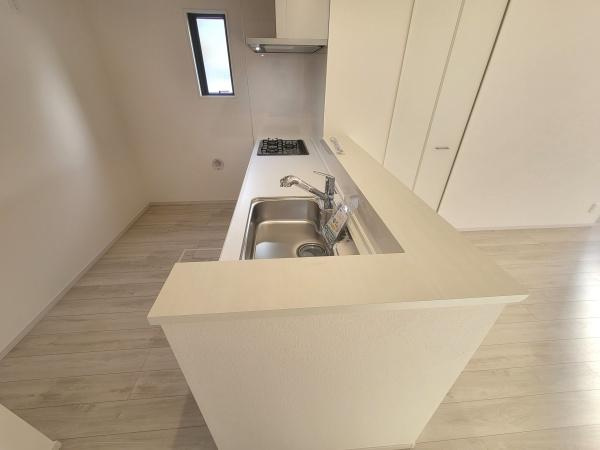 ナチュラルな色合いの床と壁がやさしい印象を与えるキッチンです。シンクやコンロがすっきりとまとまり作業スペースをしっかり確保できます。窓からの採光が明るさをプラスしています。