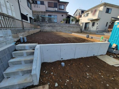 二段に分かれた敷地が特徴で空間を有効活用しやすい形状です。コンクリートの土留めがしっかりと設置されています。周囲と高低差のある立地が印象的です。階段付きでアクセスも良好に感じられます。
