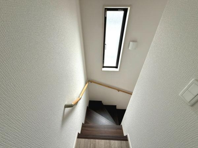 階段には縦長の窓がありしっかりとした明るさが確保されています。手すりもしっかり設置されているので移動の際も安心です。清潔感のある壁と木目の階段が調和しています。