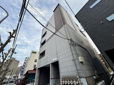 グレーの外壁がシンプルな印象の建物です。複数のガスメーターが設置されており設備が整っています。周辺には他の建物も立ち並んでおり都市部の雰囲気を感じられます。建物入口が広く利便性も期待できます。