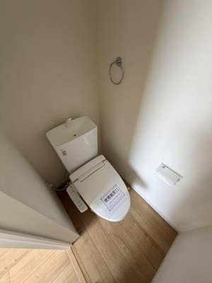 温水洗浄便座が設置されたトイレです。清潔感のある内装と明るいフロアが特徴です。必要な設備がそろっており実用的な空間です。壁付けのペーパーホルダーやタオルリングも備わっています。