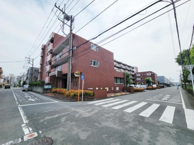 レンガ調の外観が特徴的なマンションです。角地に位置しており開放的な街並みが広がっています。建物前には緑もあり落ち着いた雰囲気が感じられます。歩道が整備されており利便性も備えています。