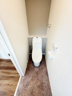 ナチュラルな色合いの床が印象的なトイレです。壁の一部には落ち着いたカラーが採用されています。ペーパーホルダーやタオルリングなど必要な設備がしっかり備わっています。シンプルで清潔感のある空間です。