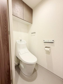 清潔感のあるトイレ空間です。手洗い一体型の便器が設置されています。壁面には収納棚があり使い勝手にも配慮されています。温水洗浄機能付きのパネルも備わっています。シンプルで使いやすい設計です。