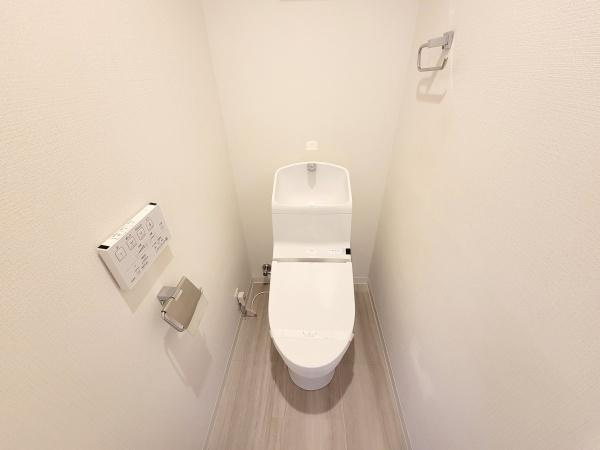 白を基調とした内装で清潔感のあるトイレです。温水洗浄便座が設置されており使い勝手も良好です。壁付けの操作パネルやペーパーホルダーも整っています。すっきりとした空間が特徴です。