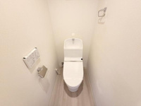 白を基調とした内装で清潔感のあるトイレです。温水洗浄便座が設置されており使い勝手も良好です。壁付けの操作パネルやペーパーホルダーも整っています。すっきりとした空間が特徴です。