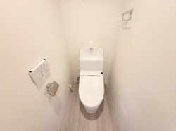 白を基調とした内装で清潔感のあるトイレです。温水洗浄便座が設置されており使い勝手も良好です。壁付けの操作パネルやペーパーホルダーも整っています。すっきりとした空間が特徴です。