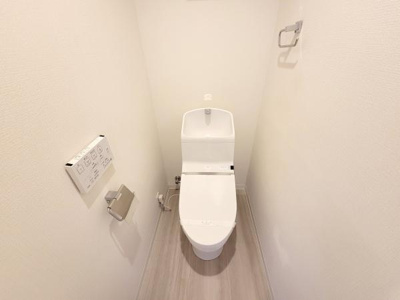 白を基調とした内装で清潔感のあるトイレです。温水洗浄便座が設置されており使い勝手も良好です。壁付けの操作パネルやペーパーホルダーも整っています。すっきりとした空間が特徴です。