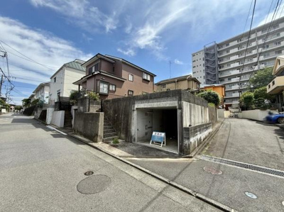 現地の前面道路は幅員が広く車の出入りがしやすい印象です。周囲には住宅やマンションが並び落ち着いた街並みが広がっています。敷地内に車庫スペースが備わっています。